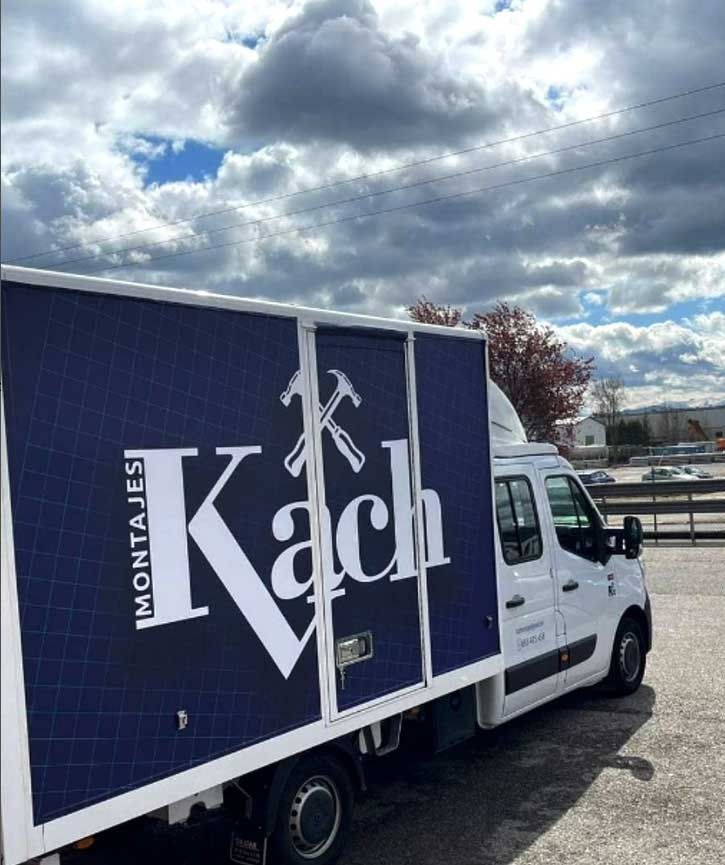 Camión de reparto blanco con el logotipo azul y blanco de Kach estacionado afuera en un día nublado.