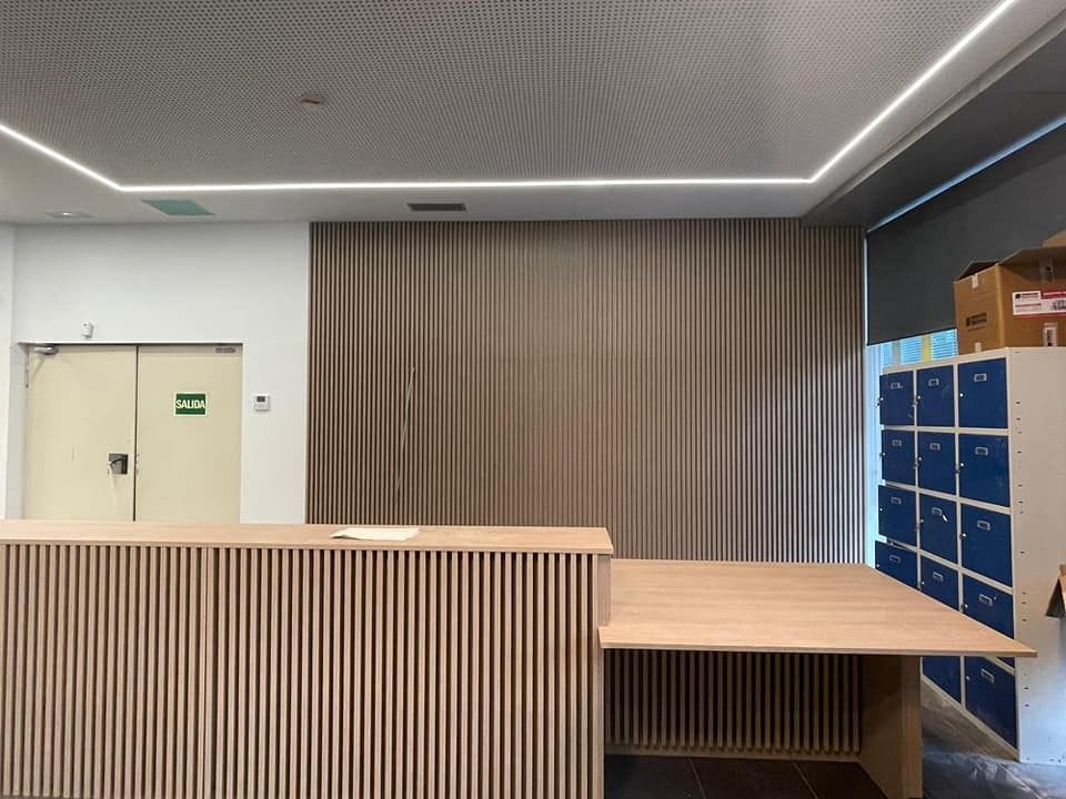 Área de recepción con un escritorio de madera clara, cortina de tono neutro y una fila de casilleros azules.