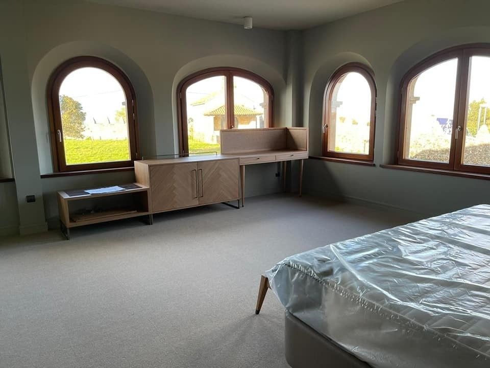 Habitación vacía con ventanas arqueadas, paredes claras y alfombra. 