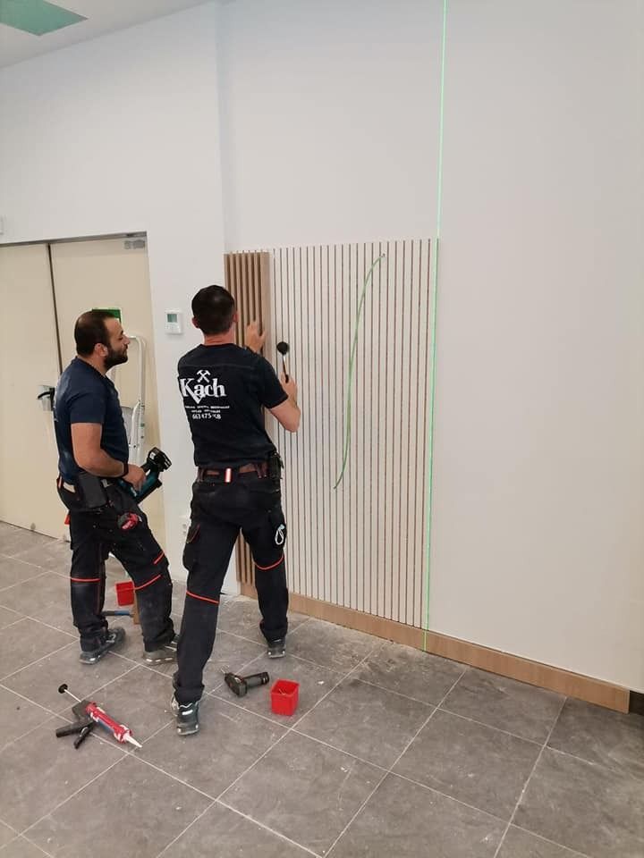 Dos trabajadores instalan un panel de madera en una pared 