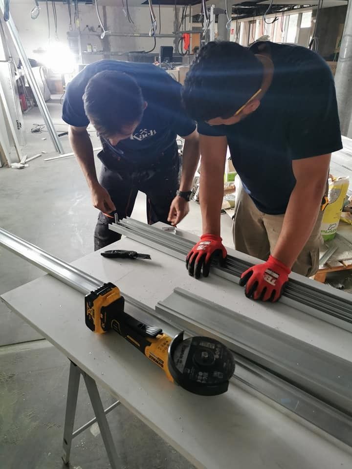 Dos personas trabajando en piezas de metal con herramientas sobre una mesa en un sitio de construcción.