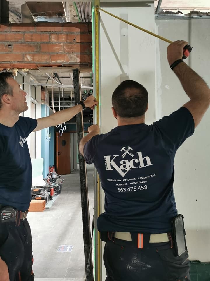 Dos trabajadores miden una pared en un sitio de construcción con una cinta métrica.