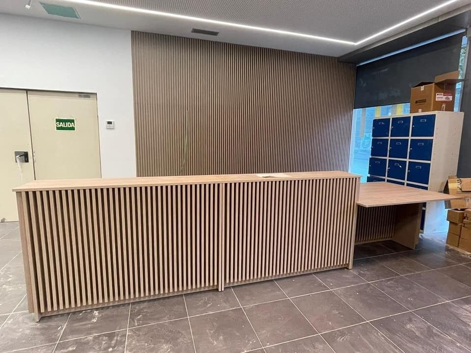 Mostrador de recepción con listones de madera, taquillas y pared estampada.