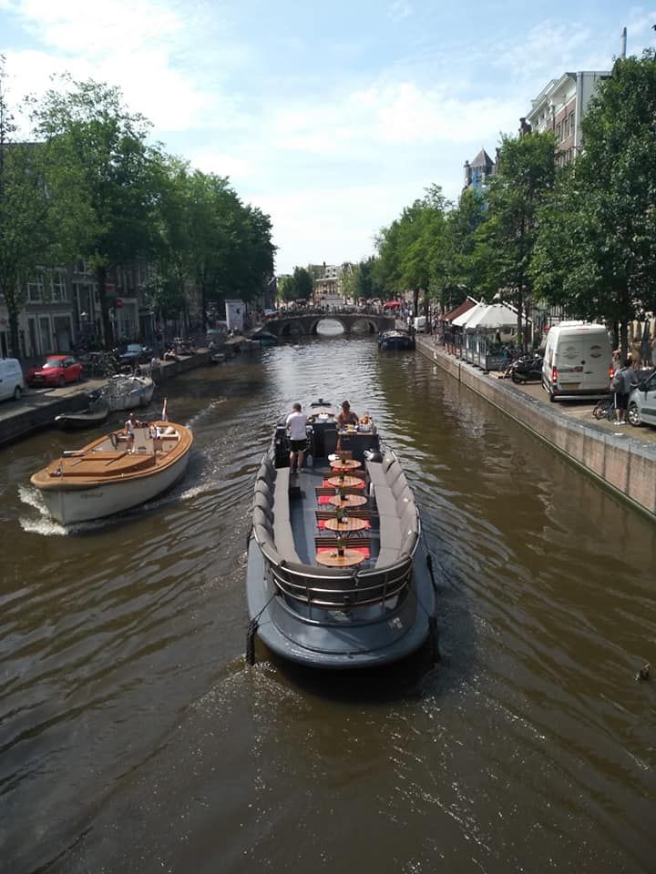 Barcos navegando por un canal en Ámsterdam, Países Bajos. Edificios a lo largo del canal. Día soleado.