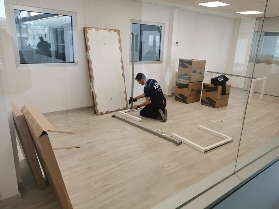 Una persona arrodillada, ensamblando un marco en una habitación vacía, con cajas de cartón cerca.