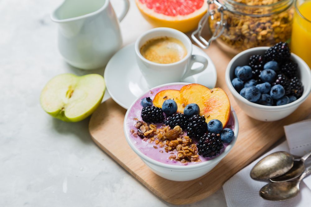 Un tazón de yogur con arándanos, duraznos y granola sobre una tabla de cortar de madera.
