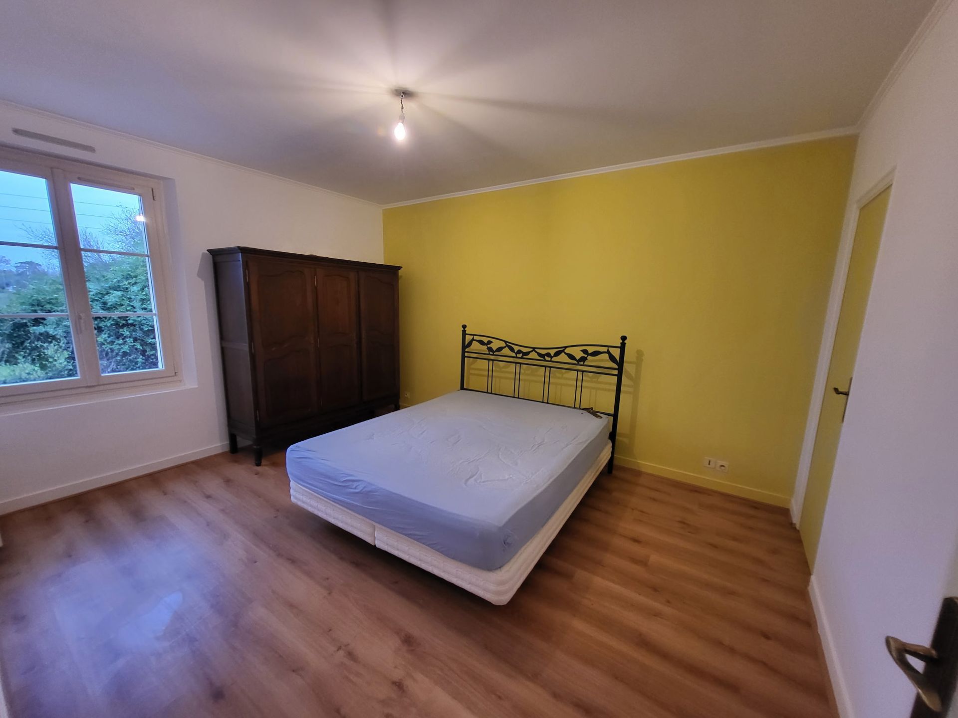 Une chambre avec un lit double, une armoire en bois foncé, un sol imitation bois et un mur d'accent.