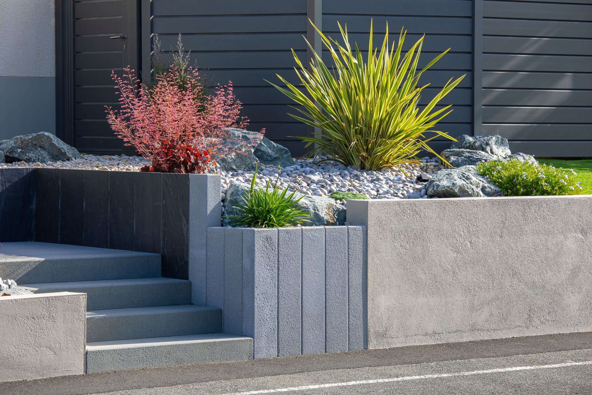 Des marches mènent à un jardin paysager moderne avec des murs en bloc et diverses plantes.