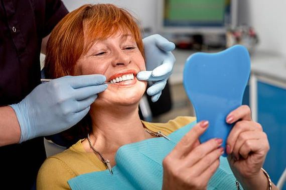 Una mujer está sentada en una silla dental mirándose los dientes en un espejo.