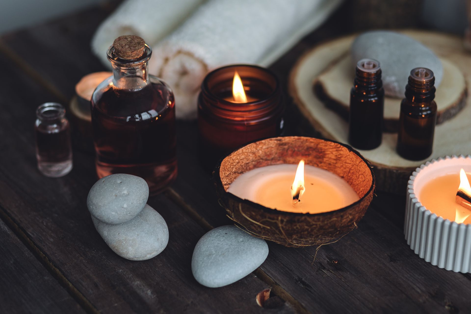 Aménagement de spa avec bougies allumées, flacons d'huiles essentielles, pierres lisses et serviettes roulées sur du bois.