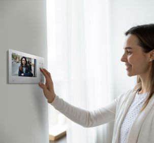 Donna che sorride allo schermo del citofono sul muro, che mostra una donna dall'altra parte della porta.