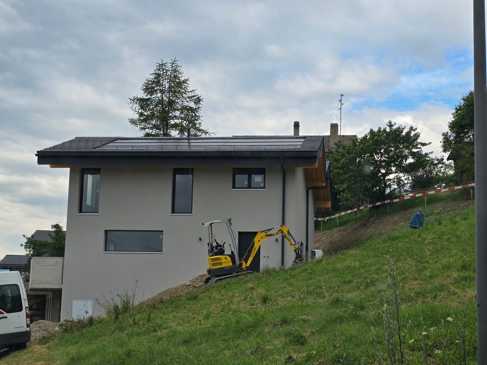Maison moderne avec panneaux solaires sur le toit, petite excavatrice à flanc de colline.