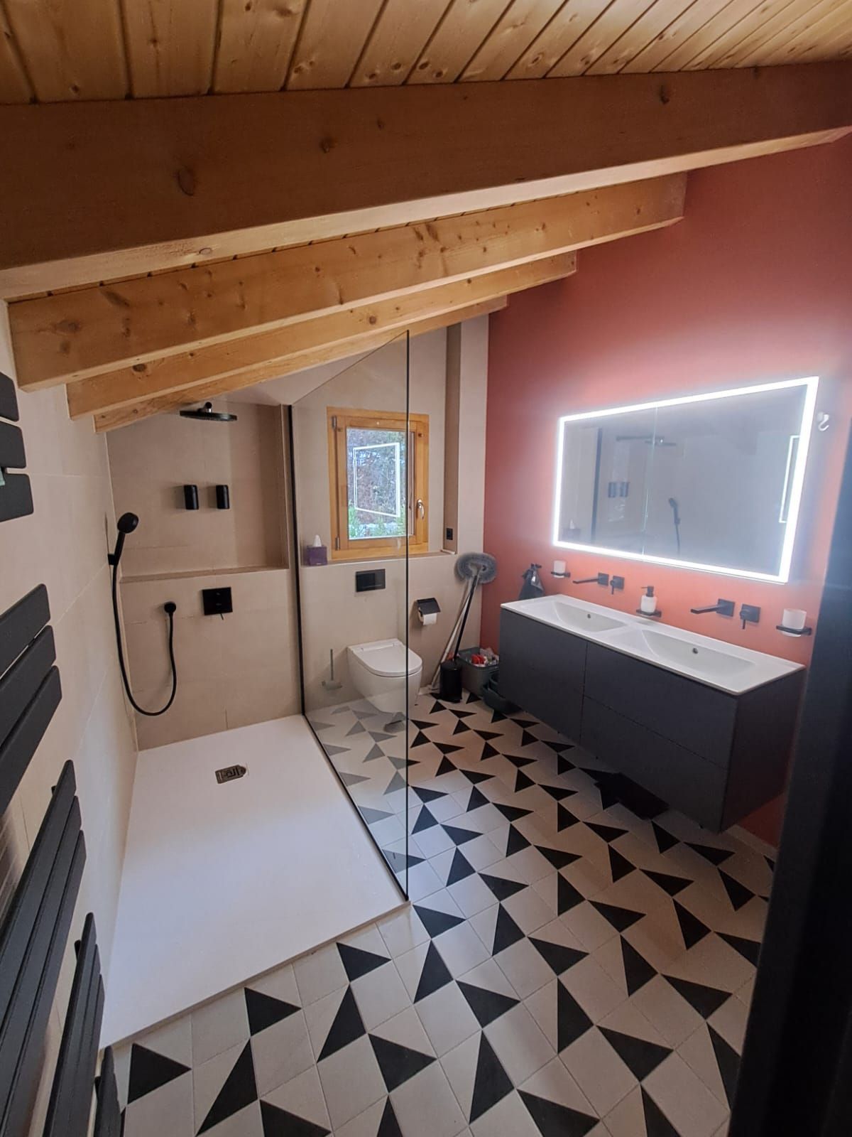 Salle de bains avec plafond en bois incliné, douche en verre, meuble-lavabo moderne et sol à motifs.