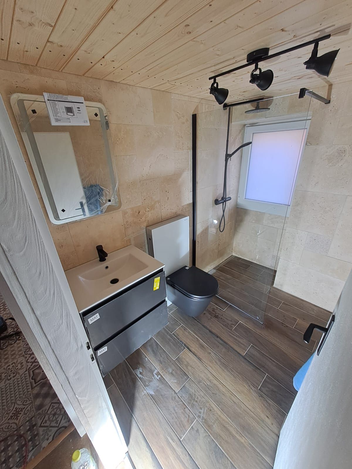 Salle de bains avec parquet, murs en pierre, toilettes, meuble-lavabo et douche.