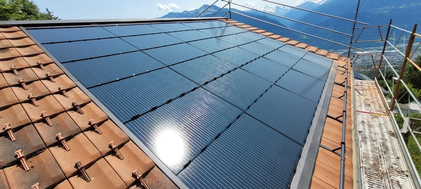 Panneaux solaires installés sur un toit de tuiles, avec une chaîne de montagnes visible en arrière-plan.