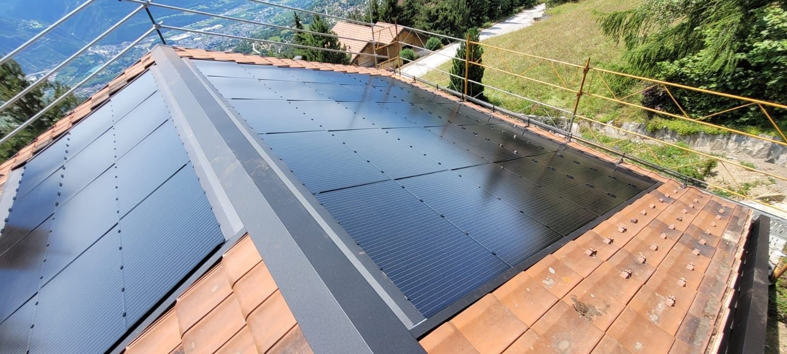 Un toit recouvert de panneaux solaires, une structure métallique et de la verdure environnante, avec un lac de montagne en arrière-plan.