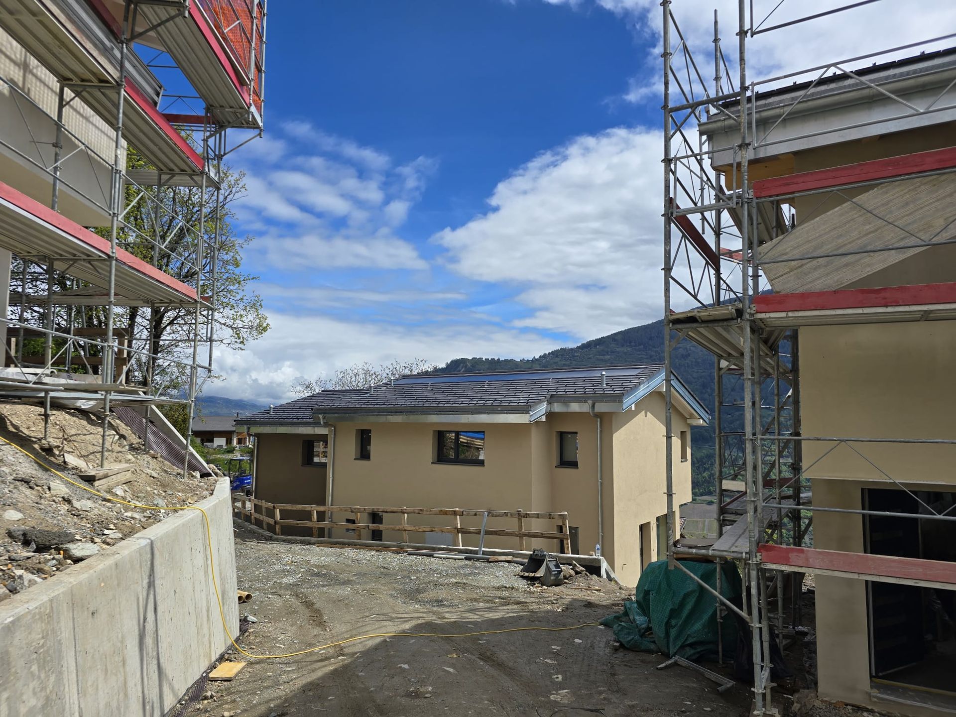 Maisons en construction avec des échafaudages sur fond de ciel bleu nuageux.
