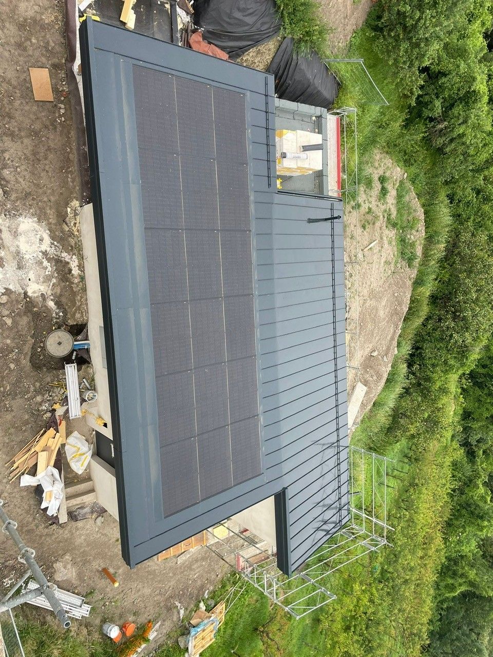 Des panneaux solaires sont installés sur un toit gris foncé. La végétation est luxuriante autour du bâtiment.