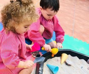 Un niño y una niña están jugando en un arenero con conos de helado.