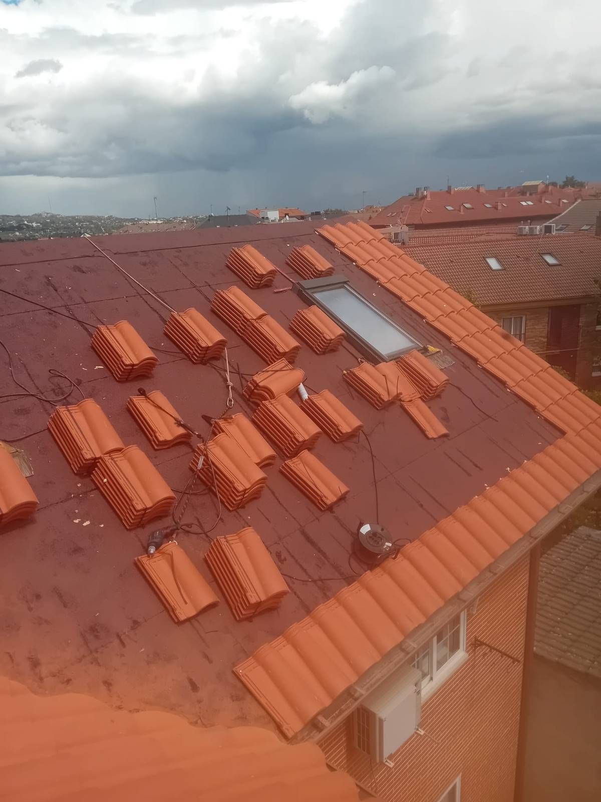 Azotea lluviosa con tejas rojas, ladrillos esparcidos y cielo nublado.