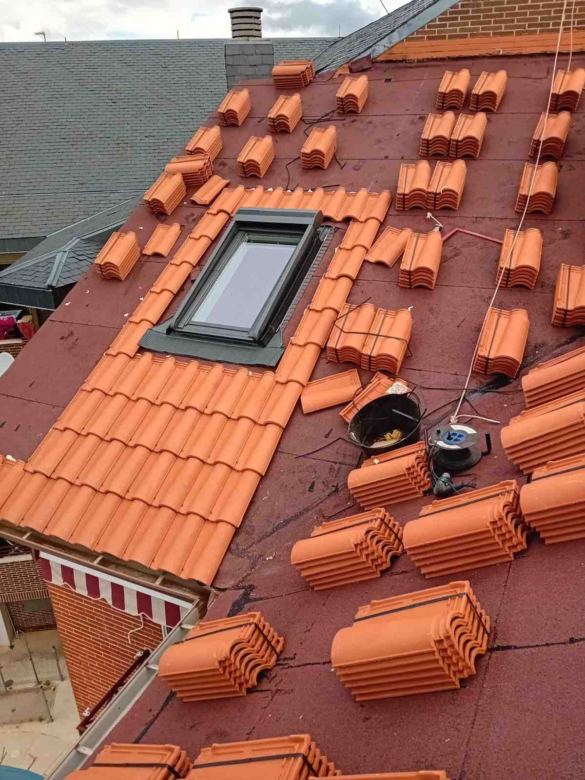 Techo en reparación con tejas naranjas, una claraboya y tejas sueltas esparcidas por la azotea.