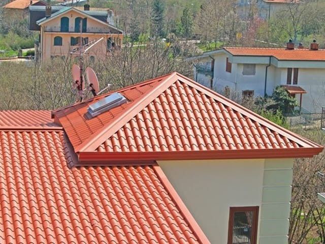 Tejados de tejas rojas con una pequeña casa en primer plano y árboles y edificios al fondo.