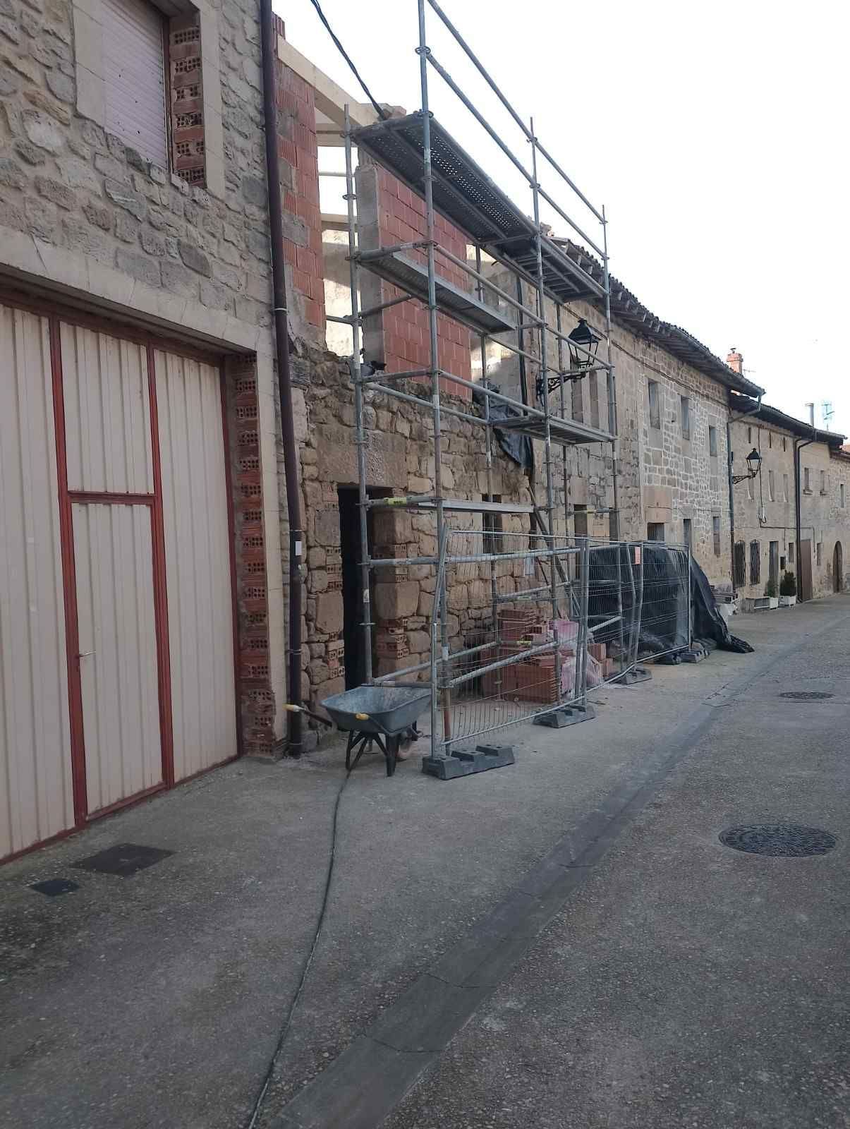 Callejón estrecho de piedra con andamios, carros y materiales de construcción junto a edificios antiguos.