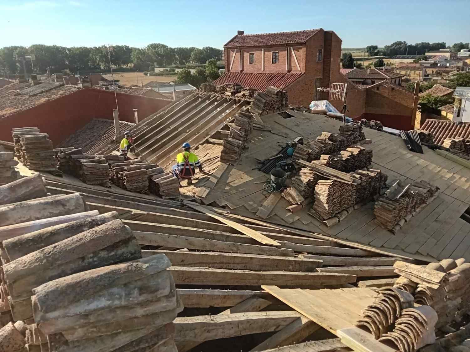 Colapso del techo con escombros y trabajadores en una obra dañada bajo cielo despejado
