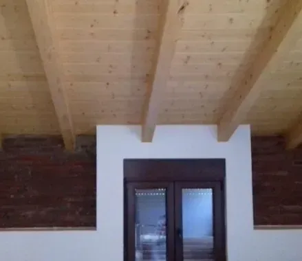 Ventana con marco blanco bajo un techo de vigas de madera, enclavada en una pared de ladrillo y yeso.