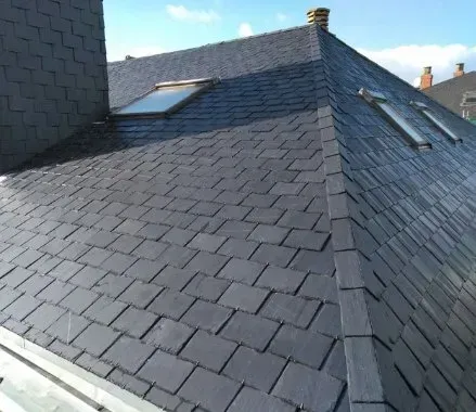 Casa con tejado de pizarra, buhardillas y chimenea.