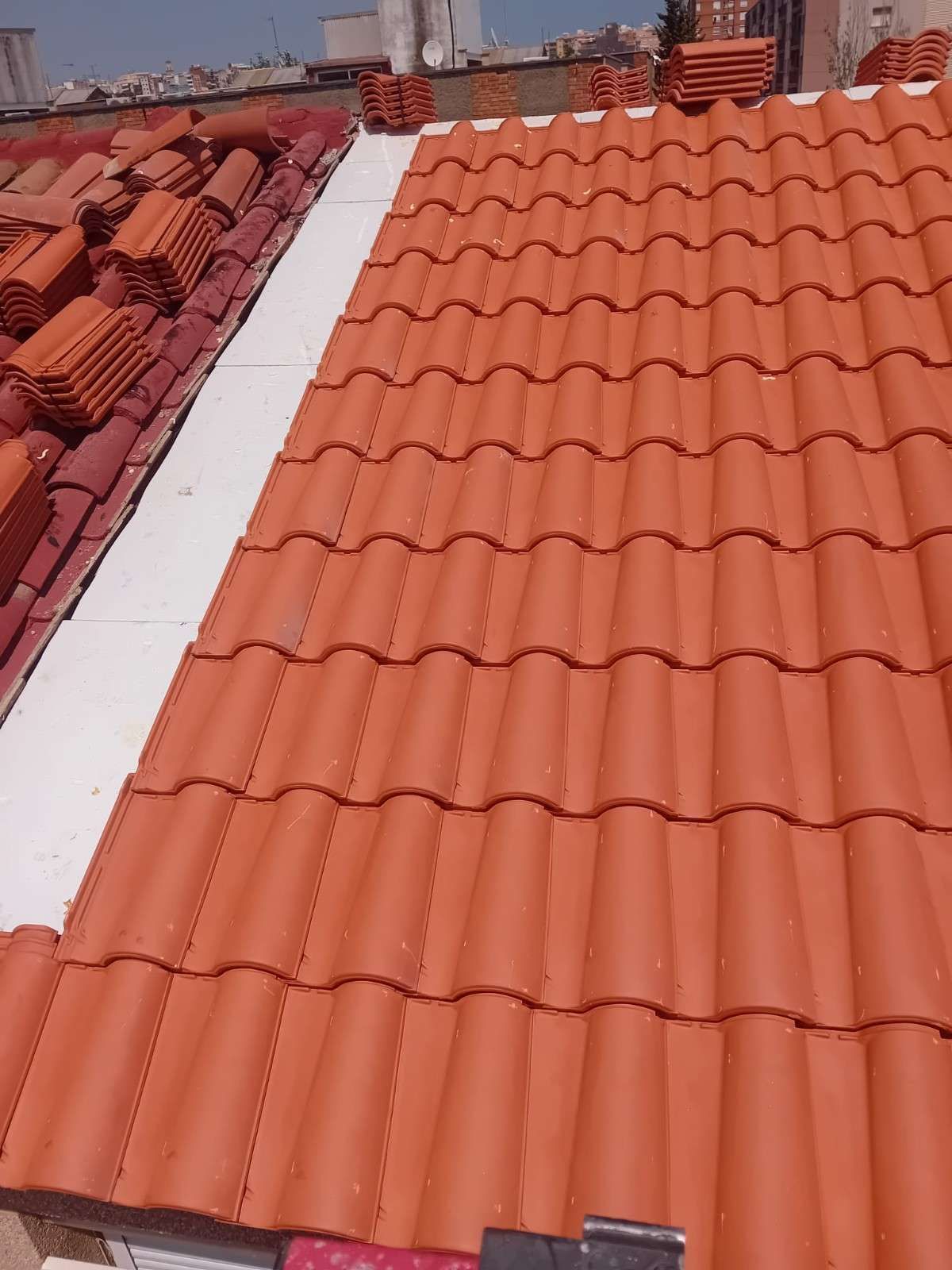 Tejado de tejas rojas con una claraboya o franja de techo blanca en un día soleado.