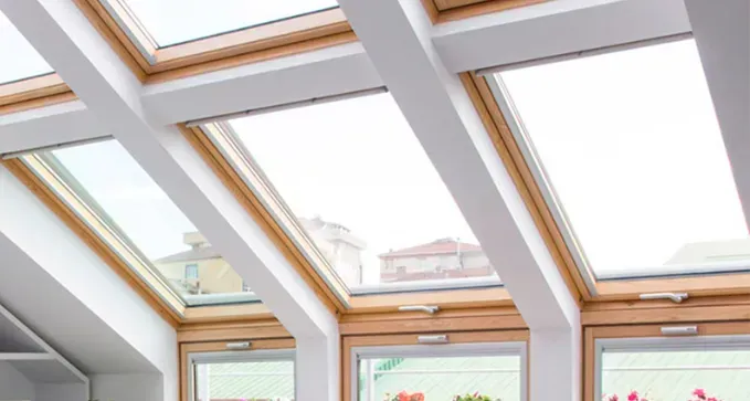 Interior con múltiples tragaluces y vigas blancas en el techo sobre ventanas con marcos de madera.