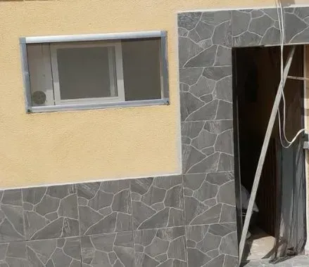 Fachada del edificio dañada con puerta y ventana rotas, paredes beige y molduras de azulejos de piedra oscura.