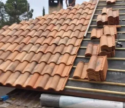 Tejas de terracota siendo instaladas en un techo inclinado, con pilas de tejas a la derecha.