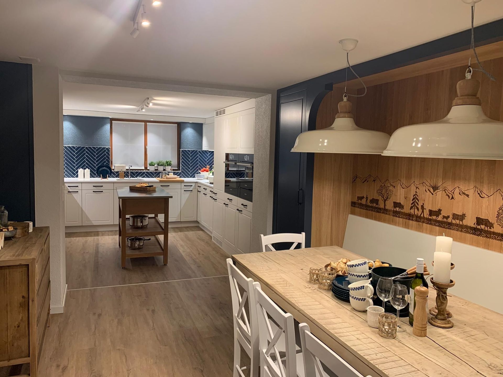 Eine Küche und ein Esszimmer mit hellen Holzböden. Die Küche hat weiße Schränke, eine blaue Küchenrückwand und eine Holzinsel