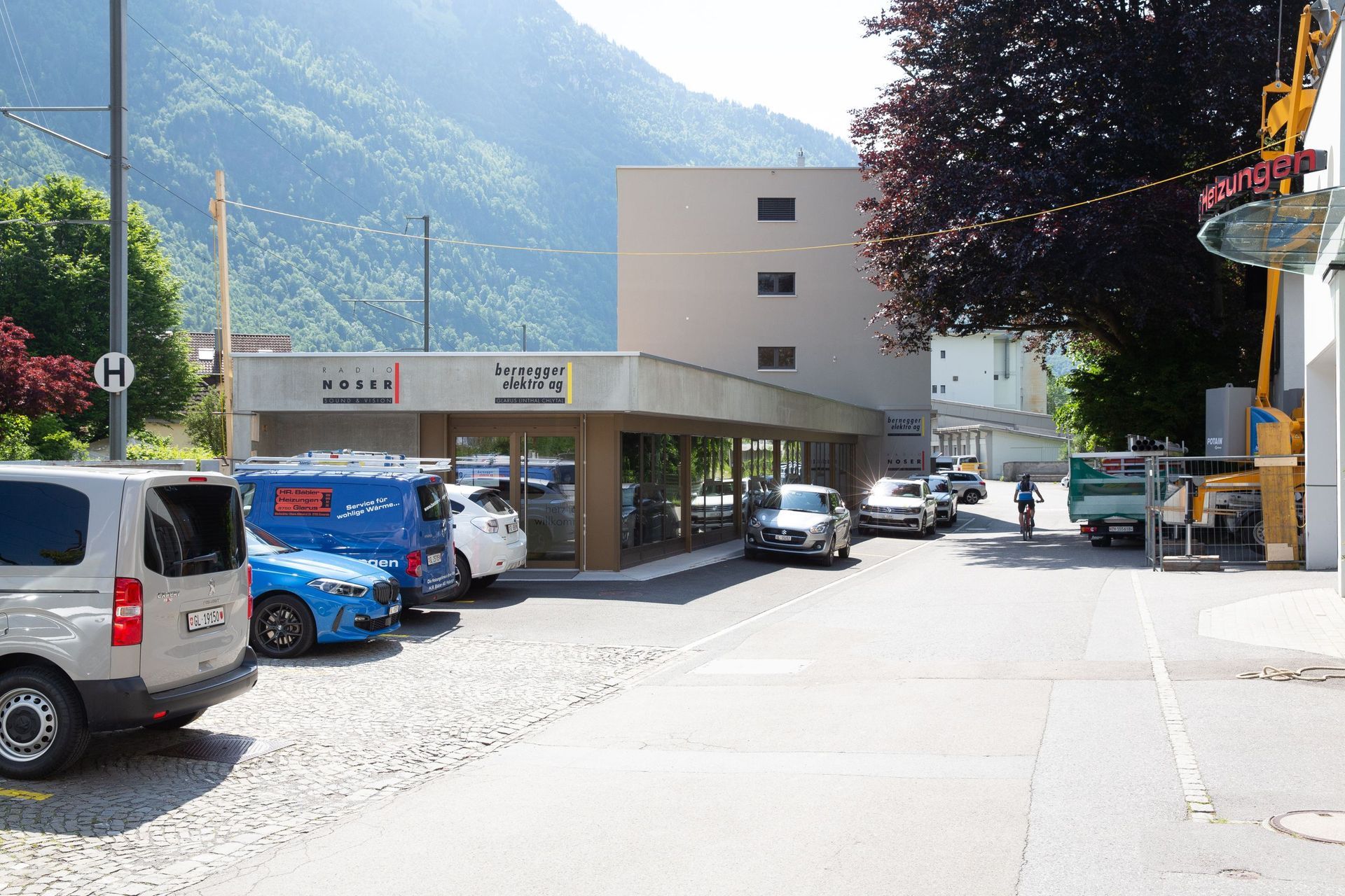 Vor einem Gebäude mit dem Schild „La Poste“ parken Autos. Im Hintergrund ist ein Berg zu sehen.