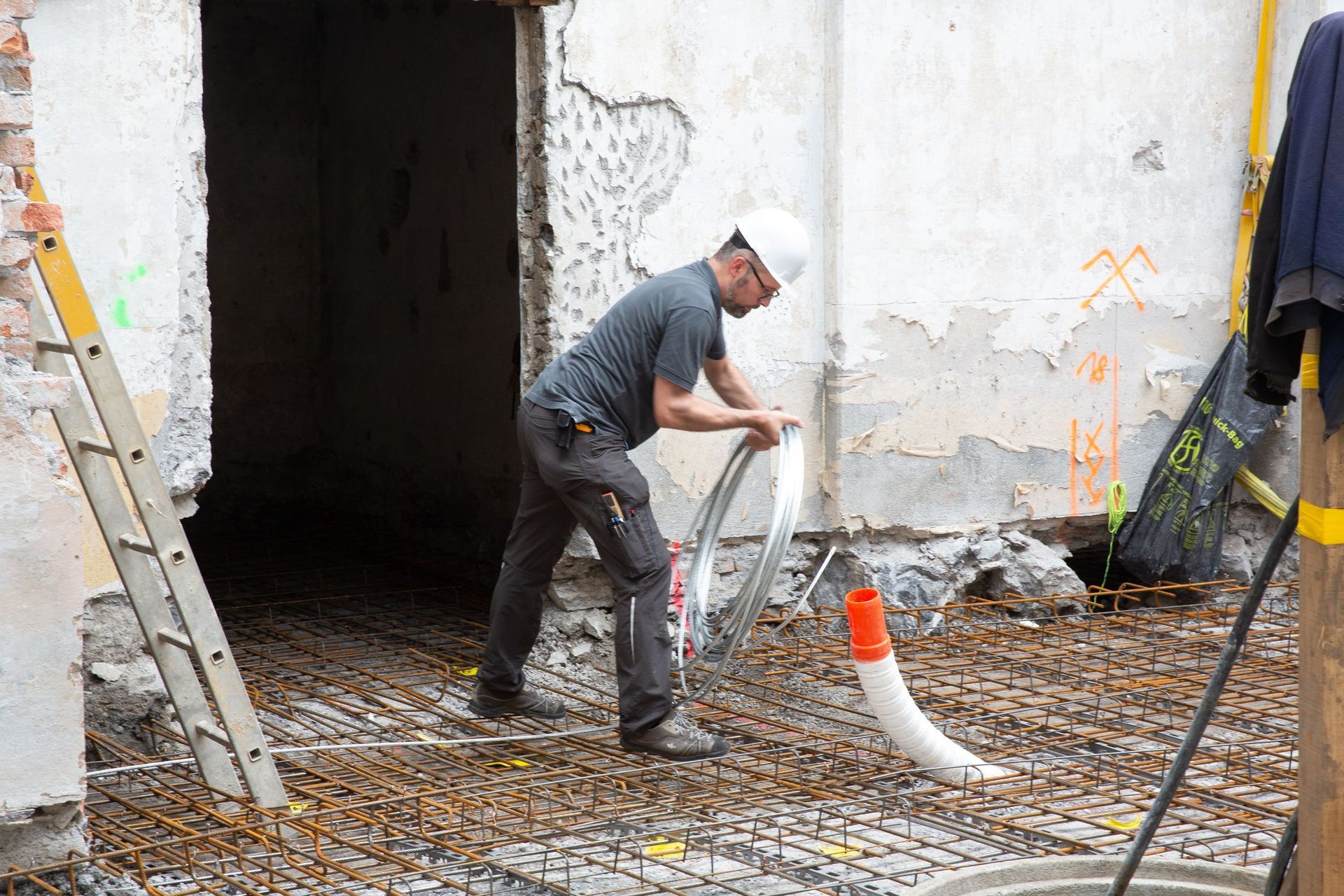 Ein Bauarbeiter zieht ein Rohr über ein Bewehrungsgitter in einem Gebäude, das gerade renoviert wird. Er trägt einen Schutzhe