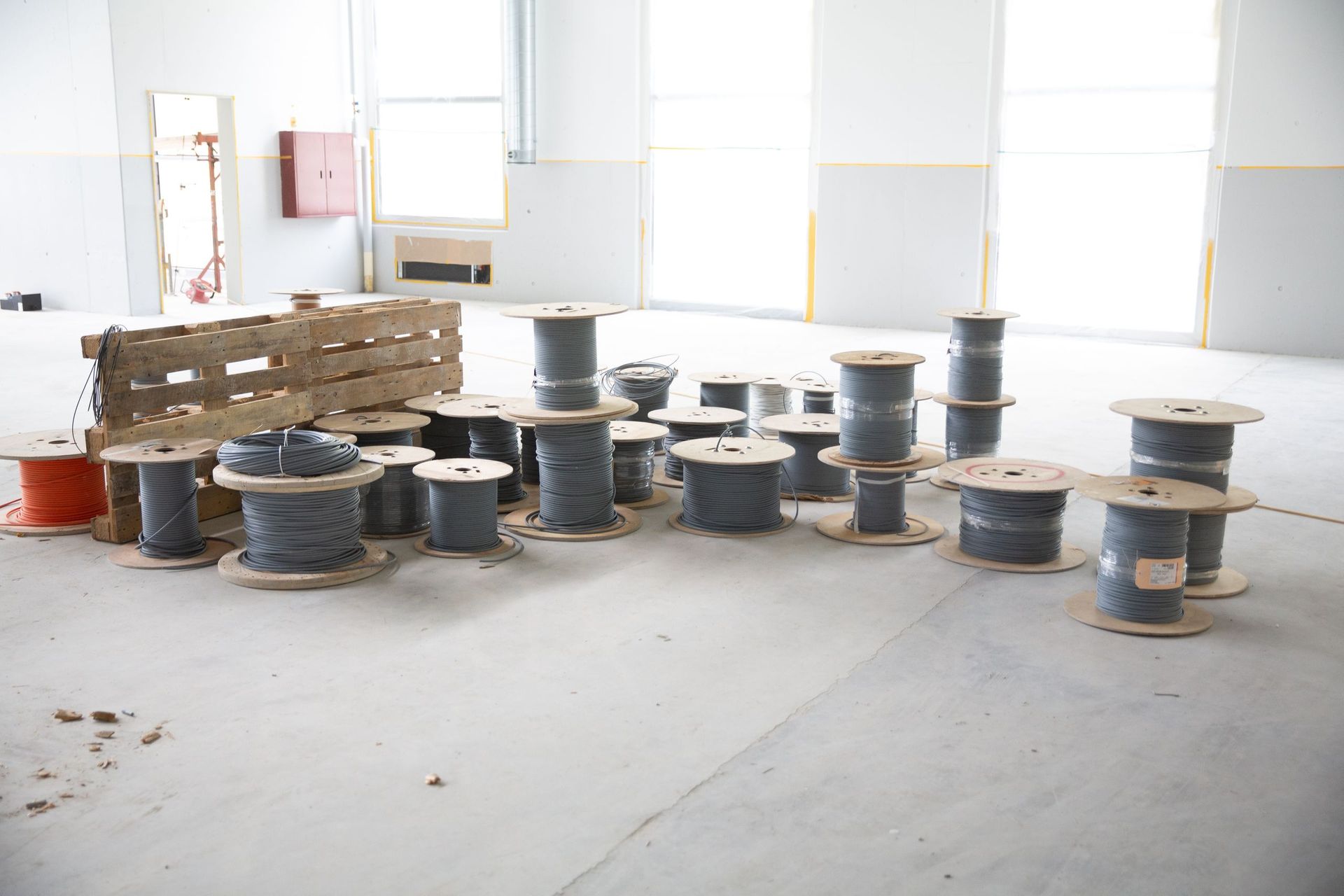 Auf dem Betonboden eines größtenteils leeren, hellen Raums liegen verstreut Spulen mit grauem Kabel. Links steht eine Holzpal