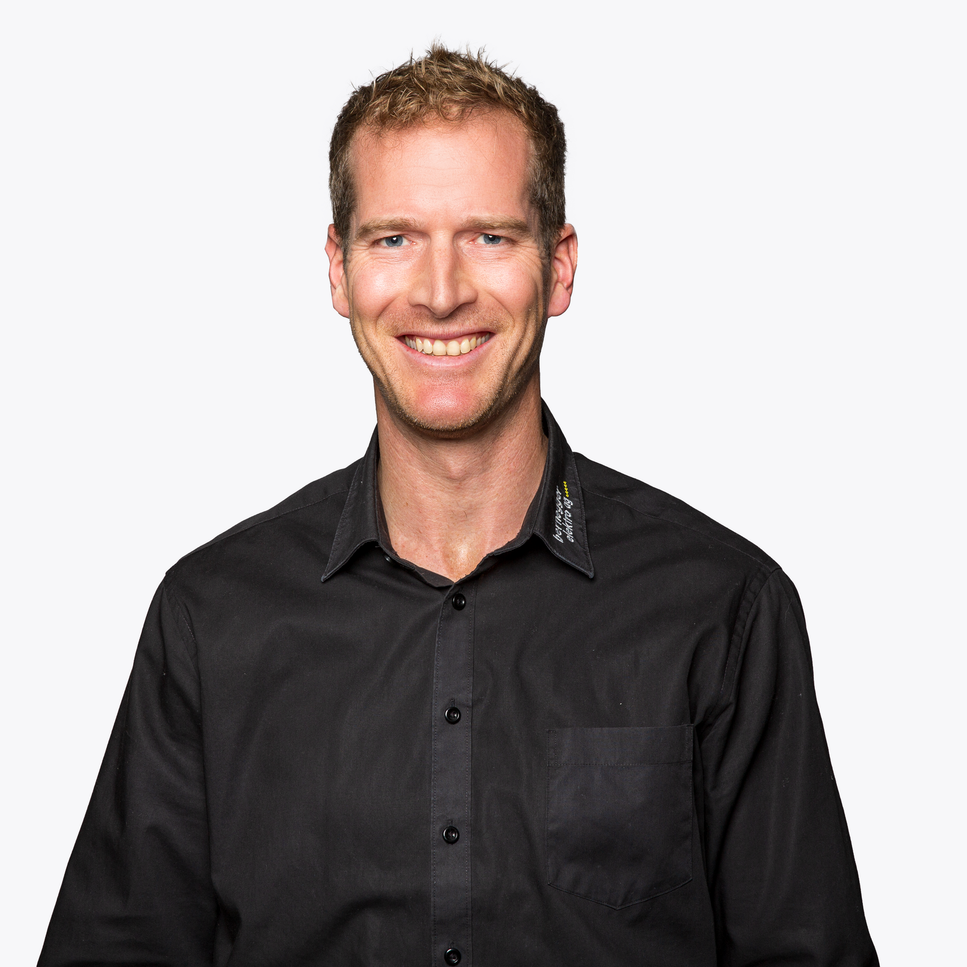 Lächelnde Frau mit blondem Haar, trägt ein dunkelgraues Button-Down-Hemd vor weißem Hintergrund.