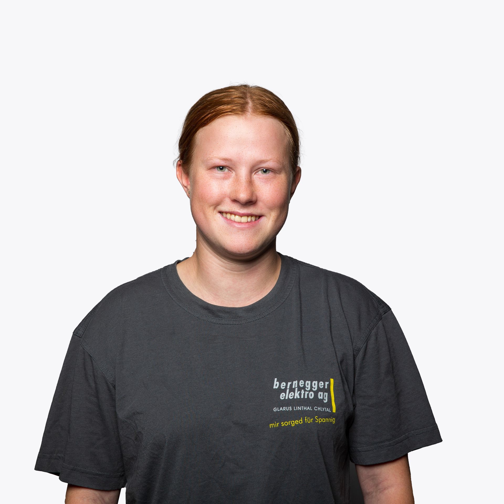 Junger Mann mit blonden Haaren und grauem T-Shirt lächelt vor weißem Hintergrund in die Kamera.
