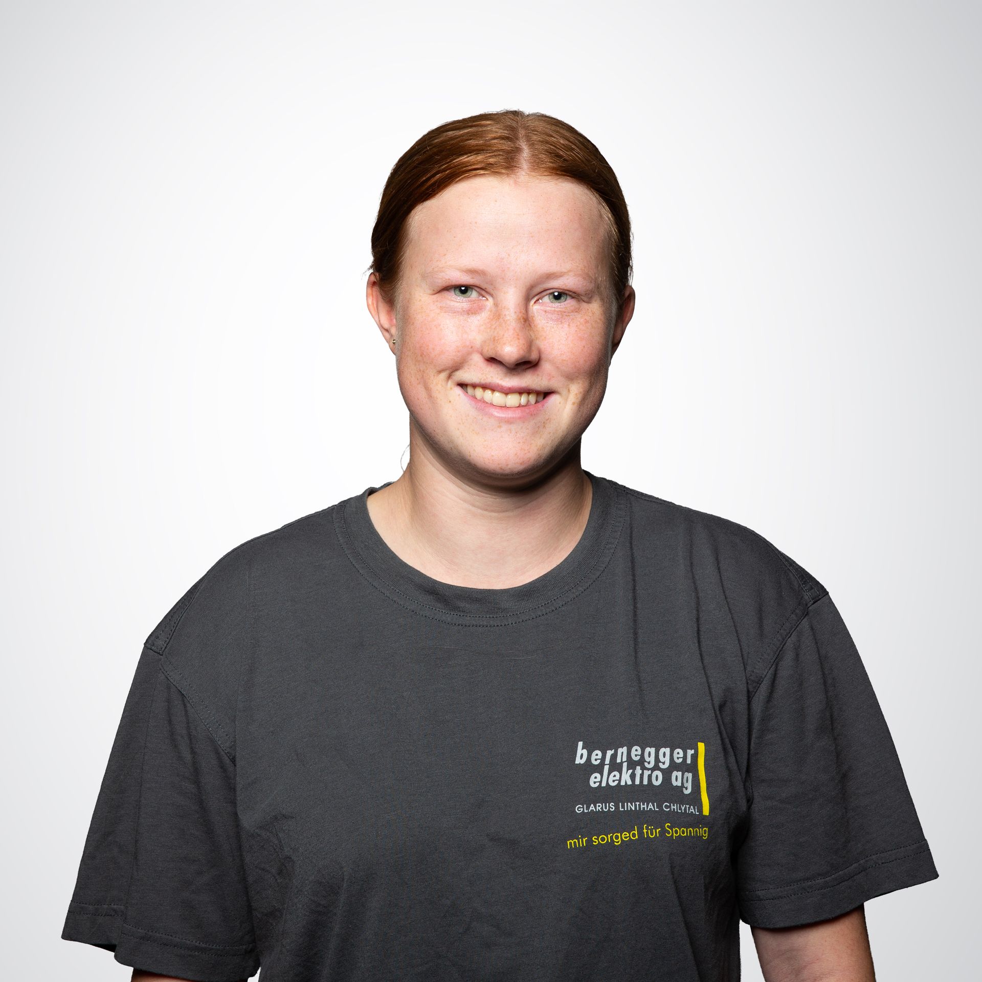 Junger Mann mit blonden Haaren und grauem T-Shirt lächelt vor weißem Hintergrund in die Kamera.
