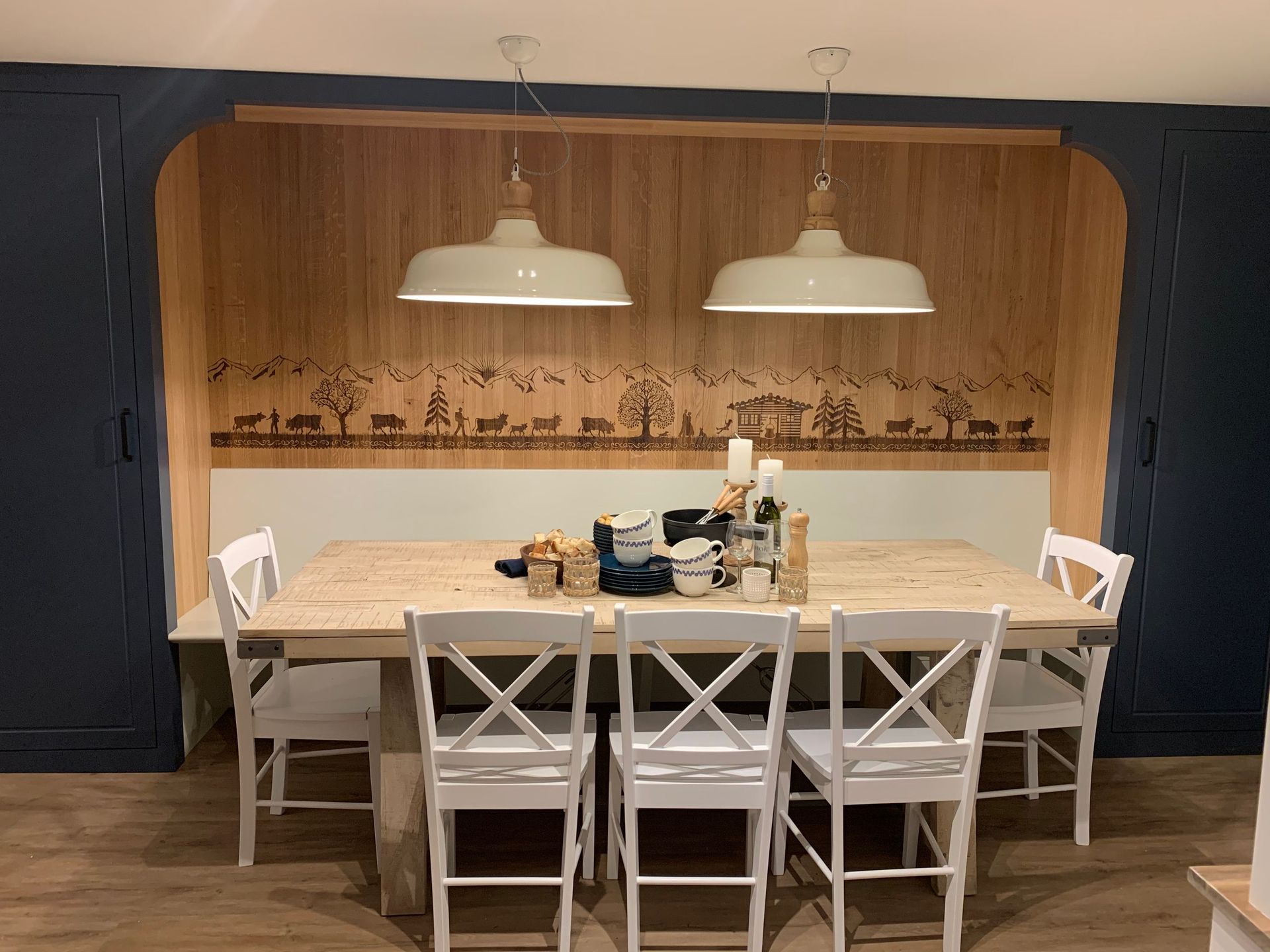 Essbereich mit einem Holztisch und weißen Stühlen in einer Nische mit Holzvertäfelung, unter zwei Hängelampen.