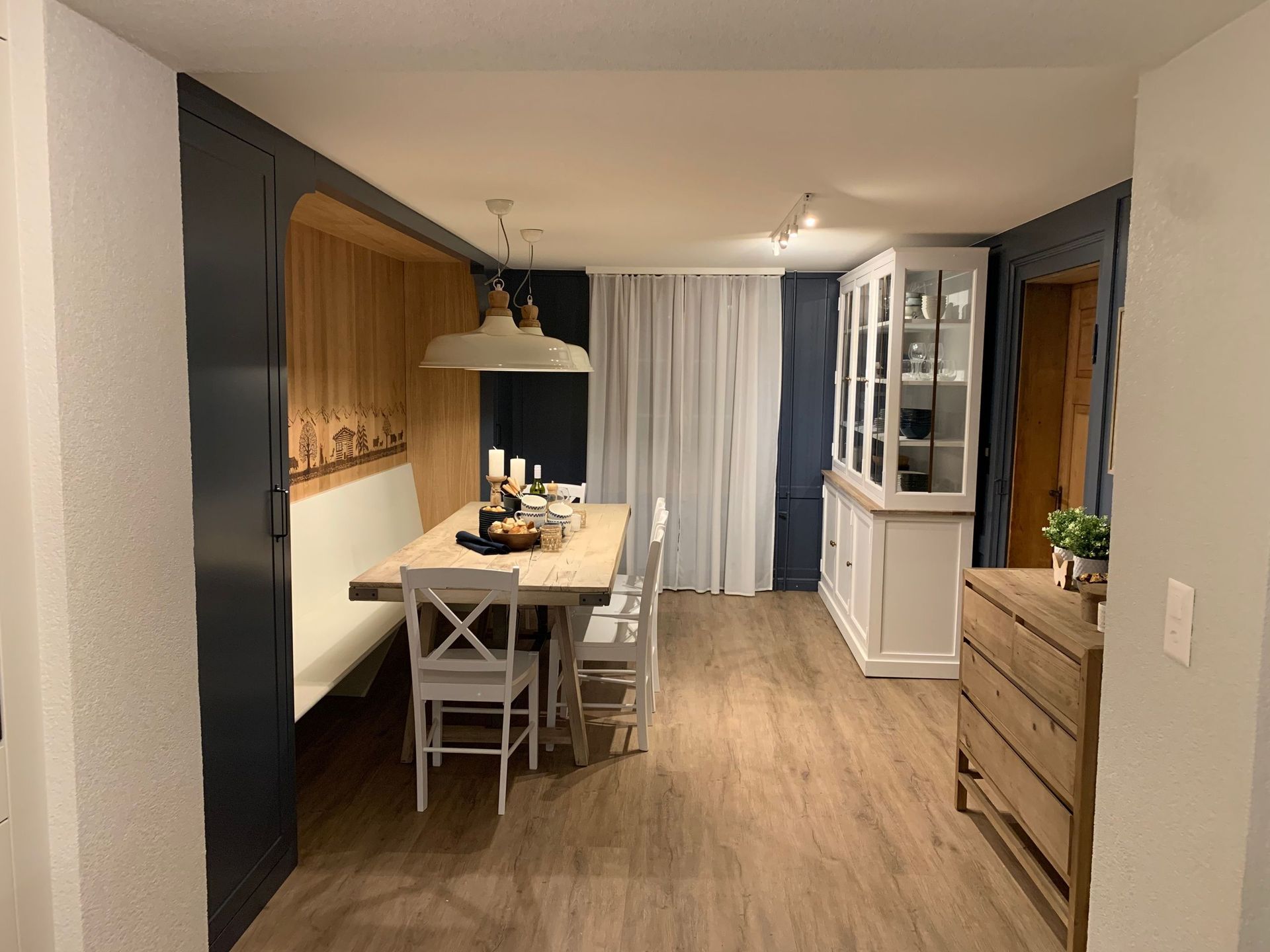 Essbereich mit holzgetäfelter Sitzecke, Tisch mit Stühlen, weißem Schrank und Holzboden. Dunkelblaue Wände.