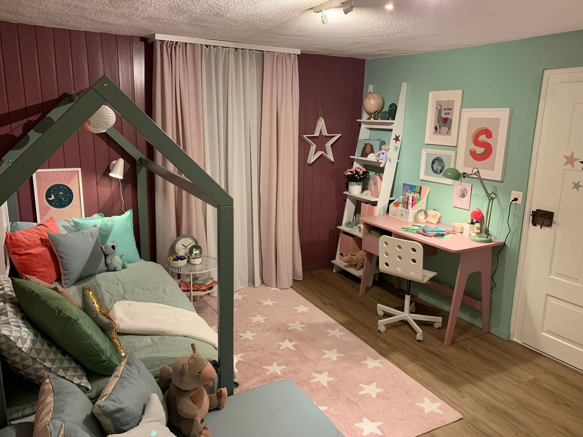 Ein farbenfrohes Kinderzimmer mit einem hausförmigen Bett, einem Schreibtisch und Sternendekorationen in Grün-, Rosa- und Wei