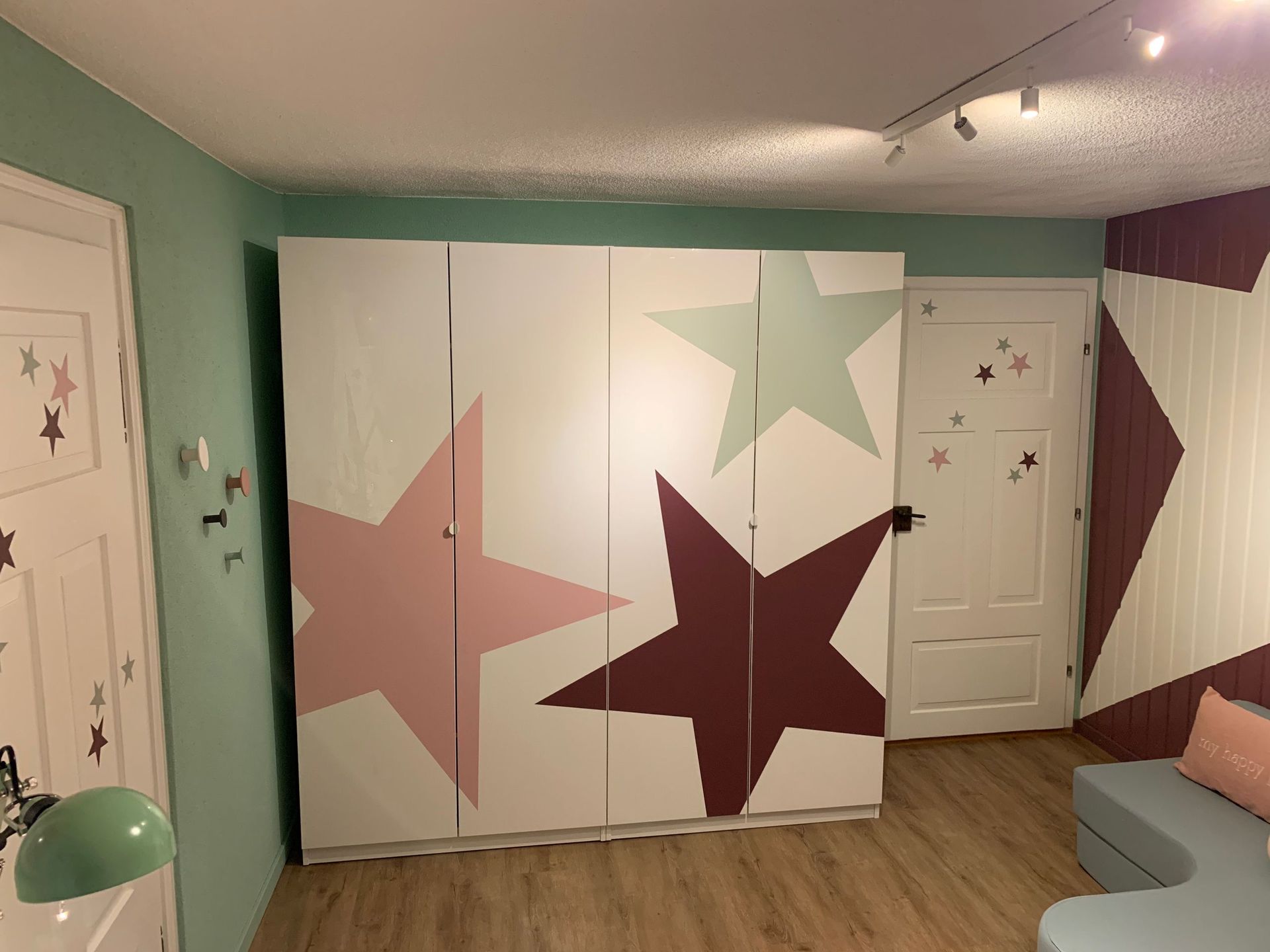 Ein Kinderzimmer mit einem weißen Kleiderschrank, der mit großen pastellfarbenen Sternen verziert ist, einer Tür mit Sternena