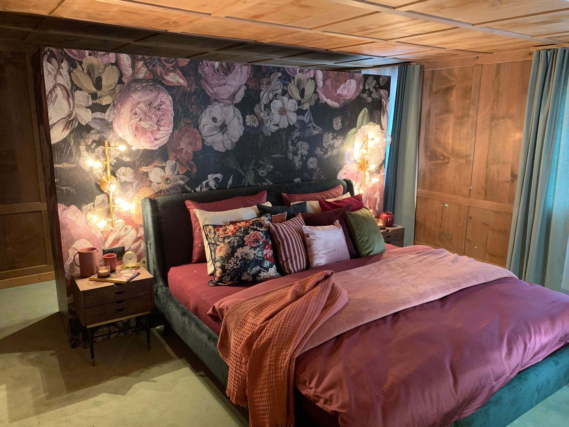 Gemütliches Schlafzimmer mit Blumentapete, burgunderfarbenem Bett und Holzvertäfelung. Warme Beleuchtung und dekorative Kiss.