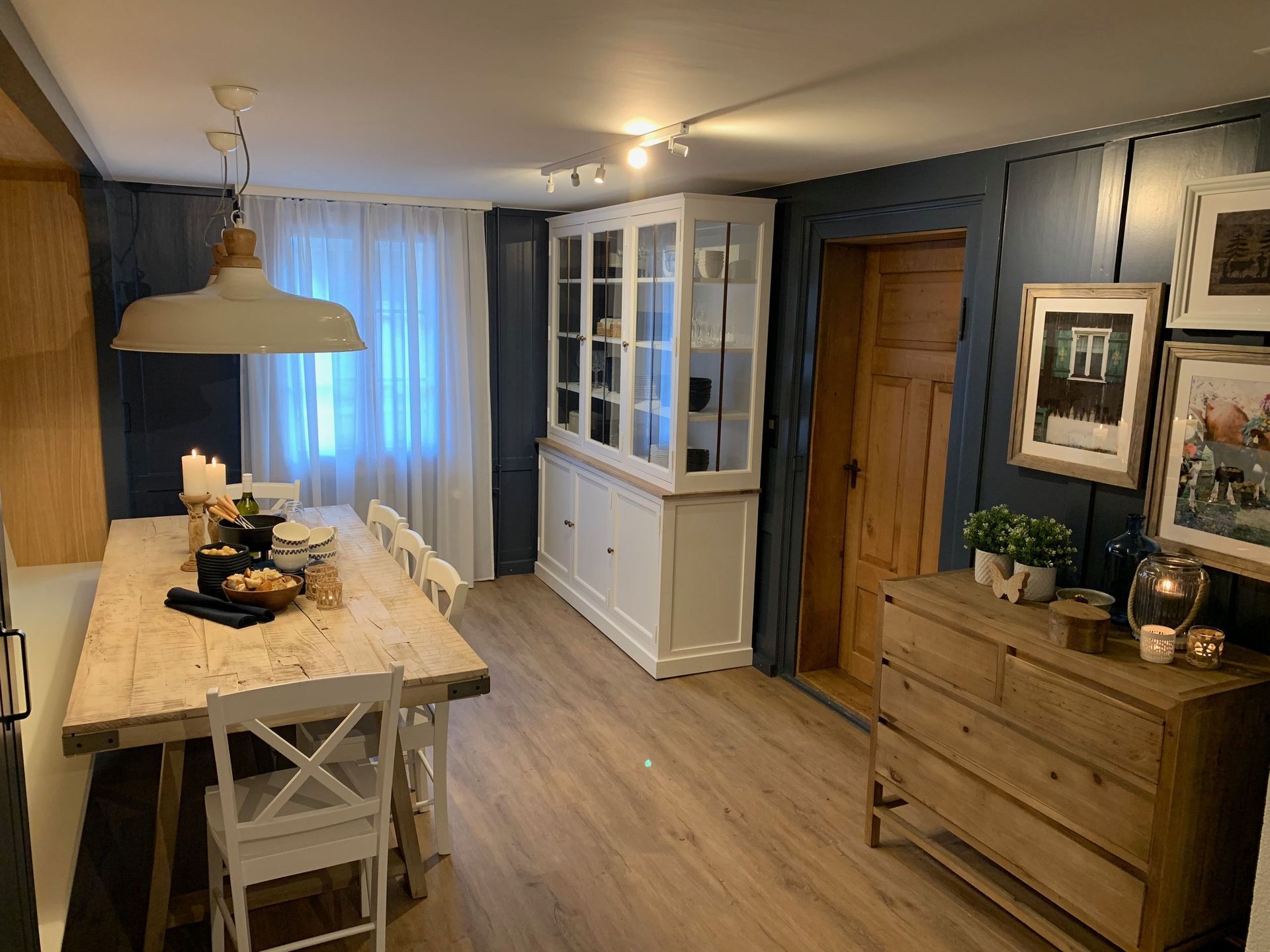 Rustikales Esszimmer: weißer Bauerntisch mit Stühlen, weißer Schrank, Holzkommode und blau getäfelte Wände.