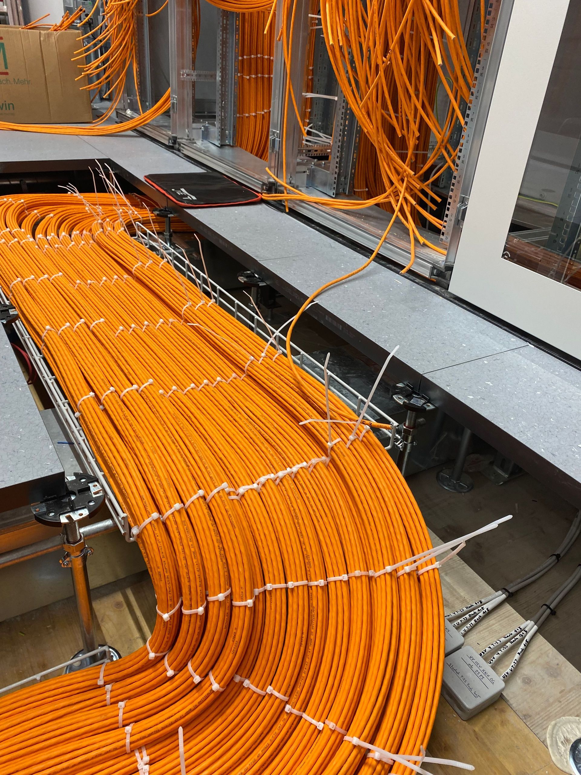 Ein großes Bündel leuchtend orangefarbener Kabel, ordentlich angeordnet, schlängelt sich in einer Industrieumgebung entlang e