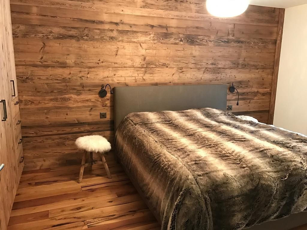 Schlafzimmer mit einer holzgetäfelten Akzentwand hinter einem Bett mit einer Kunstfelldecke. In der Nähe steht ein flauschig