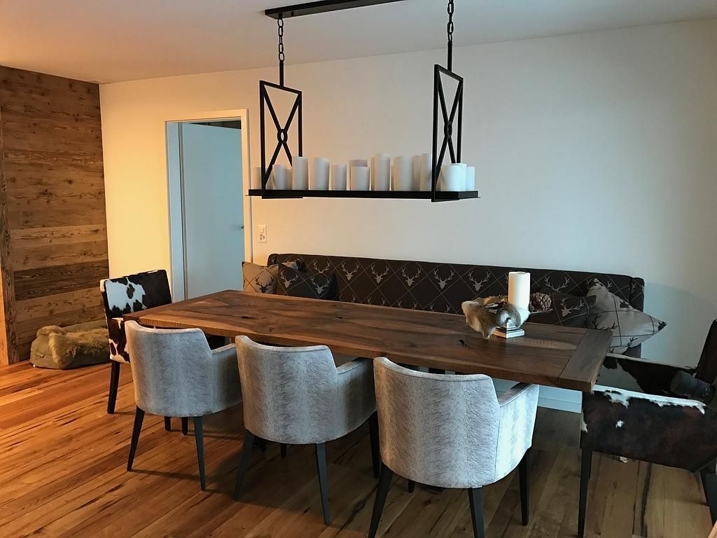 Esszimmer mit Holztisch, gemusterten Stühlen, einer dunklen Bank und einem modernen Kronleuchter.